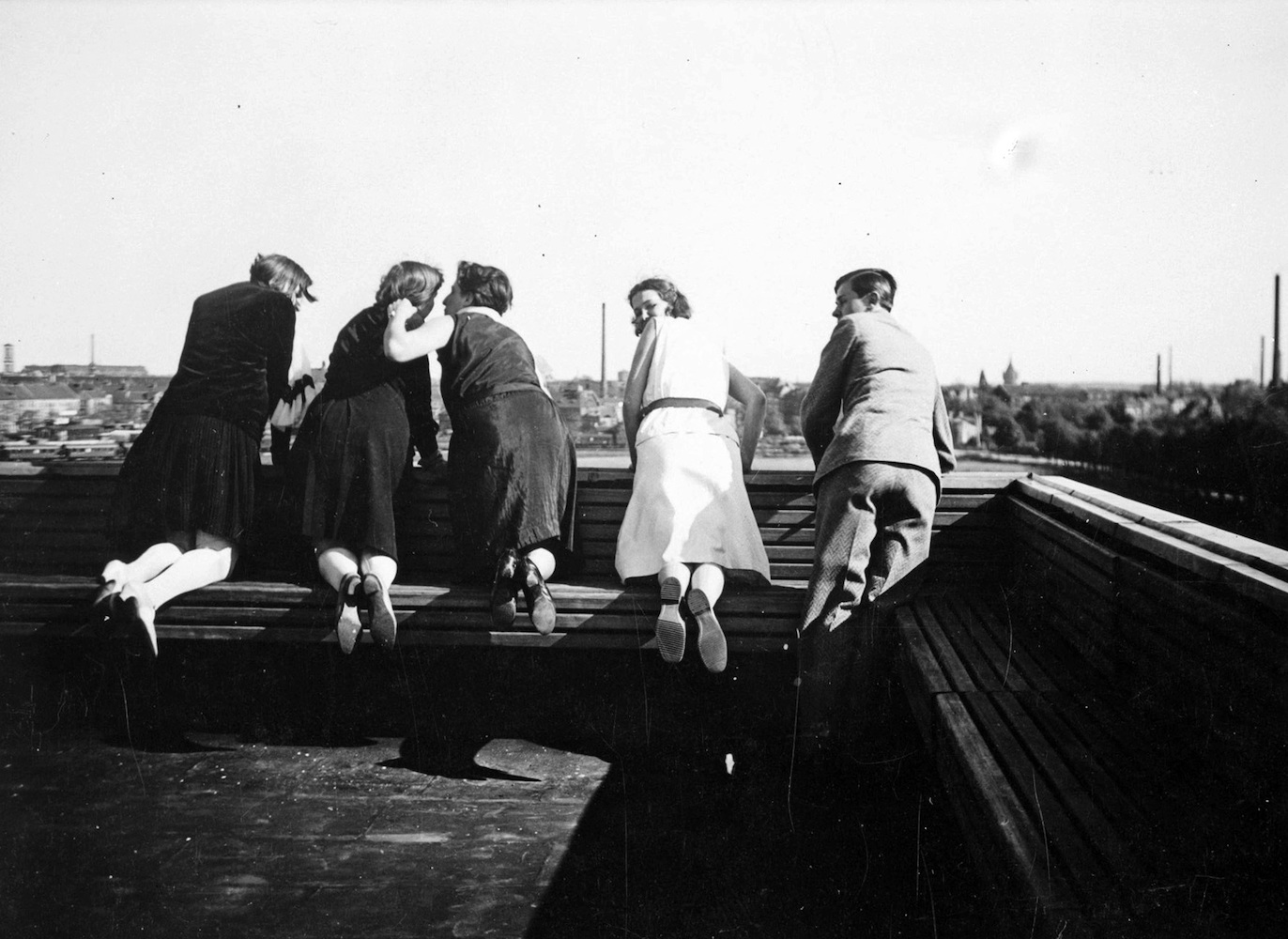 Auf den Dachbänken des Bauhauses knieende Personen in Rückenansicht