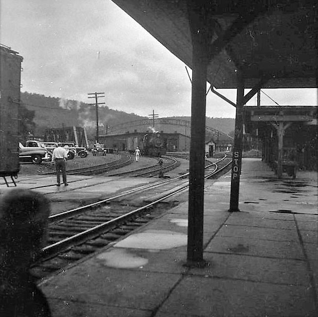 Bahnhof auf dem Land mit Dampflok und Wartenden, fotografiert vom Bahnsteig aus