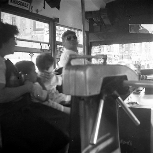 Bus Driver and Woman with two Toddlers photographed inside a bus, Turnstile in the foreground