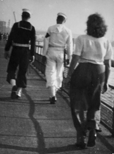 Two Sailors followed by a young Woman walking on the Promenade