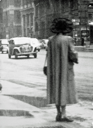 Straßenszene. Frau im Mantel mit großem Hut an der Bordsteinkante