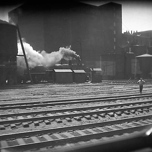 Blick aus einem Zug auf Gleise mit Dampflok und Gleisarbeiter