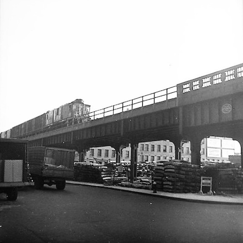 Freight Train on an elevated Track over Storage Yard, two Trucks